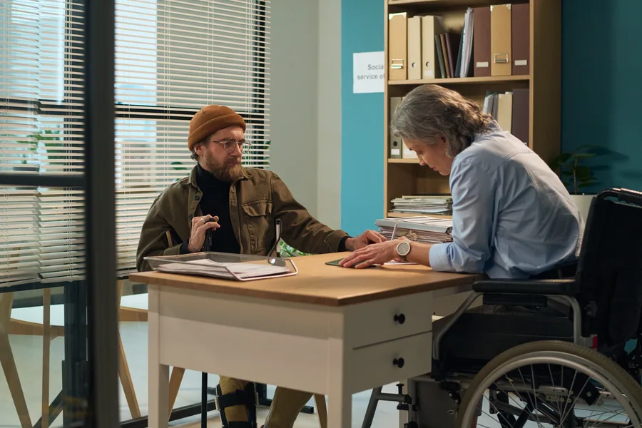 Caseworker meeting a client who uses a wheelchair at an office desk